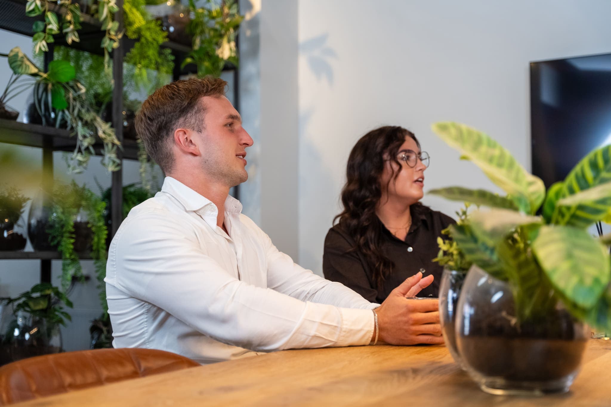 Man en vrouw luisteren aan een houten tafel tijdens een bijeenkomst, voor ConnectYou