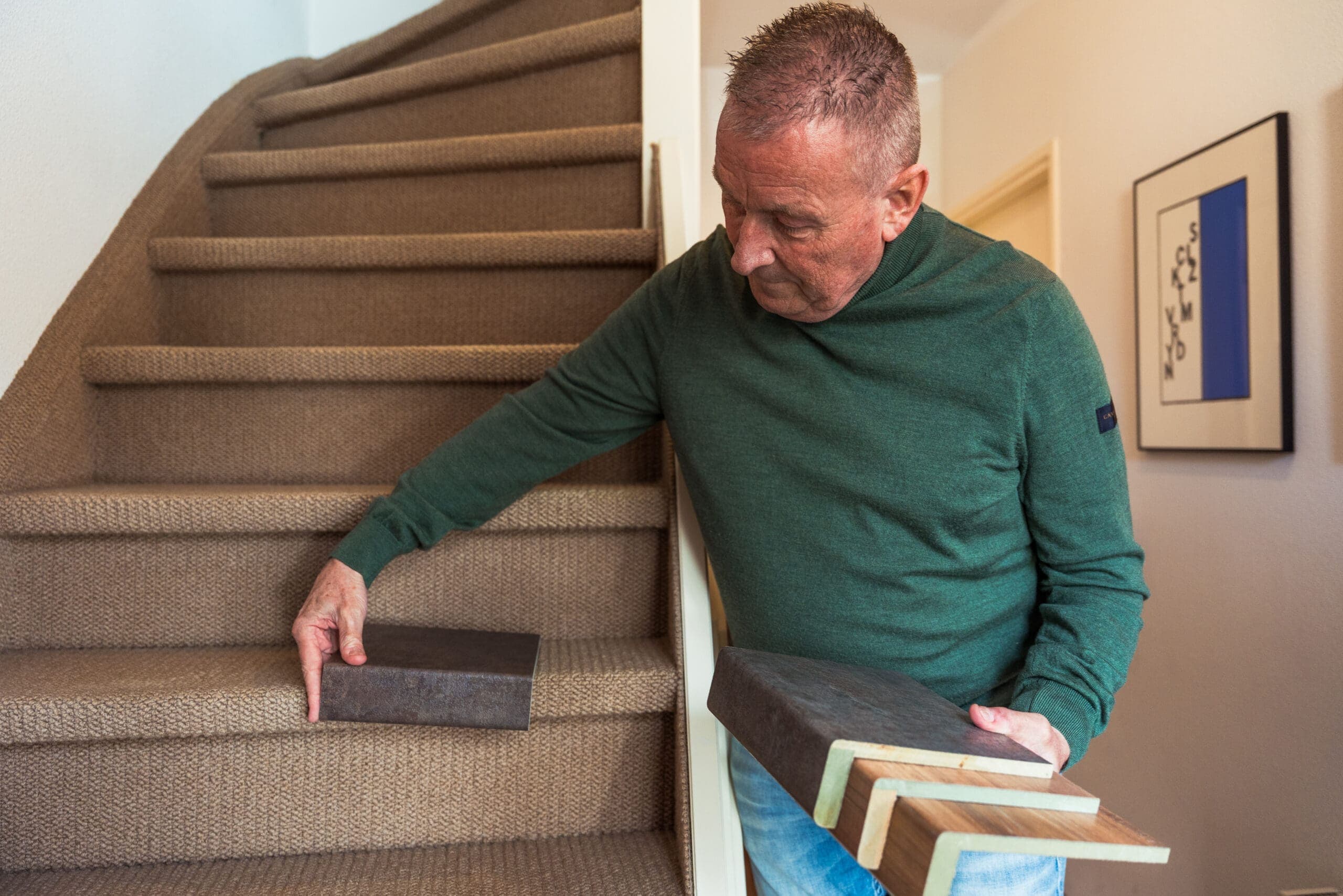 Man houdt houten trapmonsters vast naast een trap met tapijt, TrapXpress