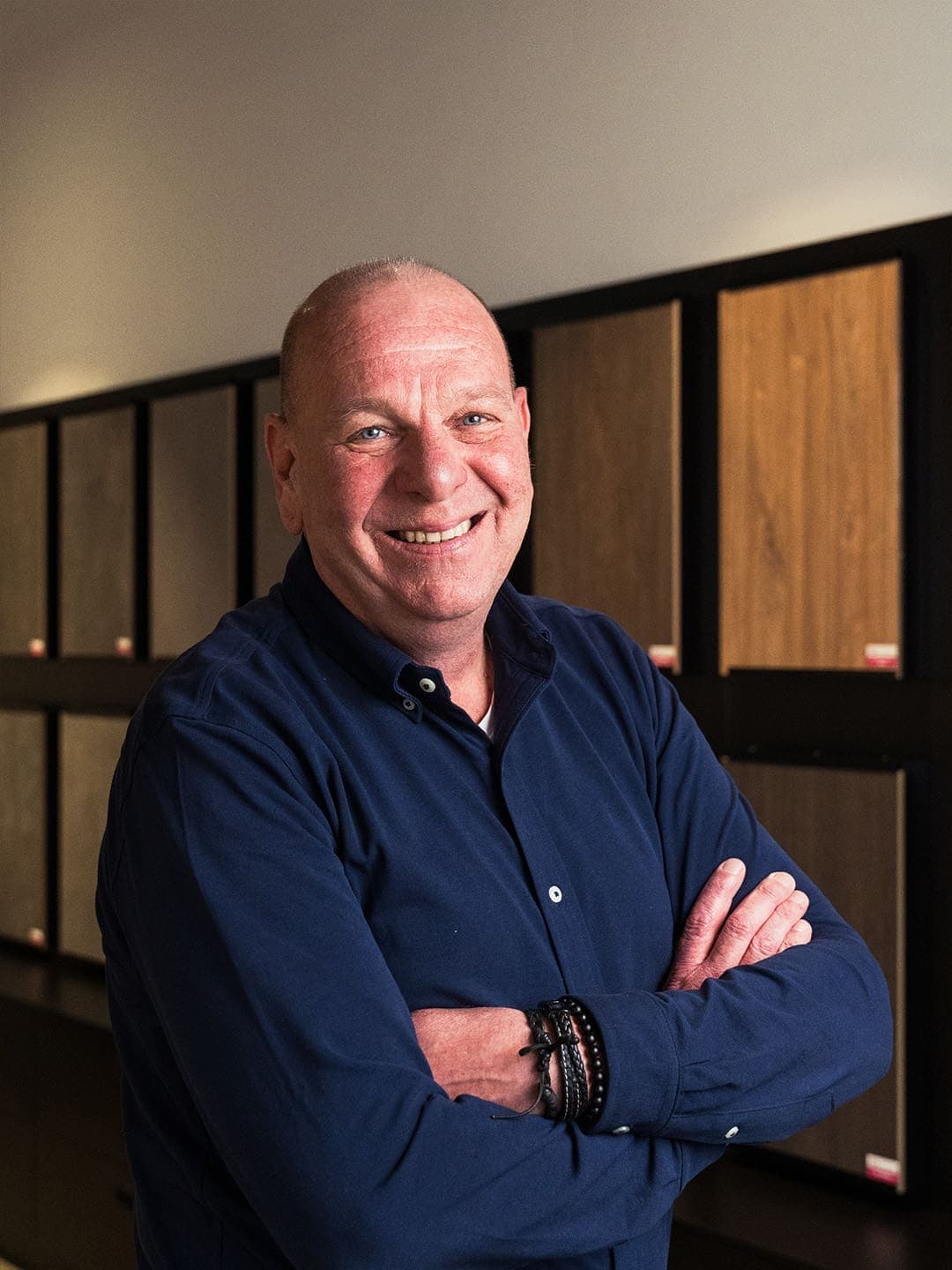 Traprenovatie-adviseur Hans met gekruiste armen voor een wand met houtmonsters, TrapXpress